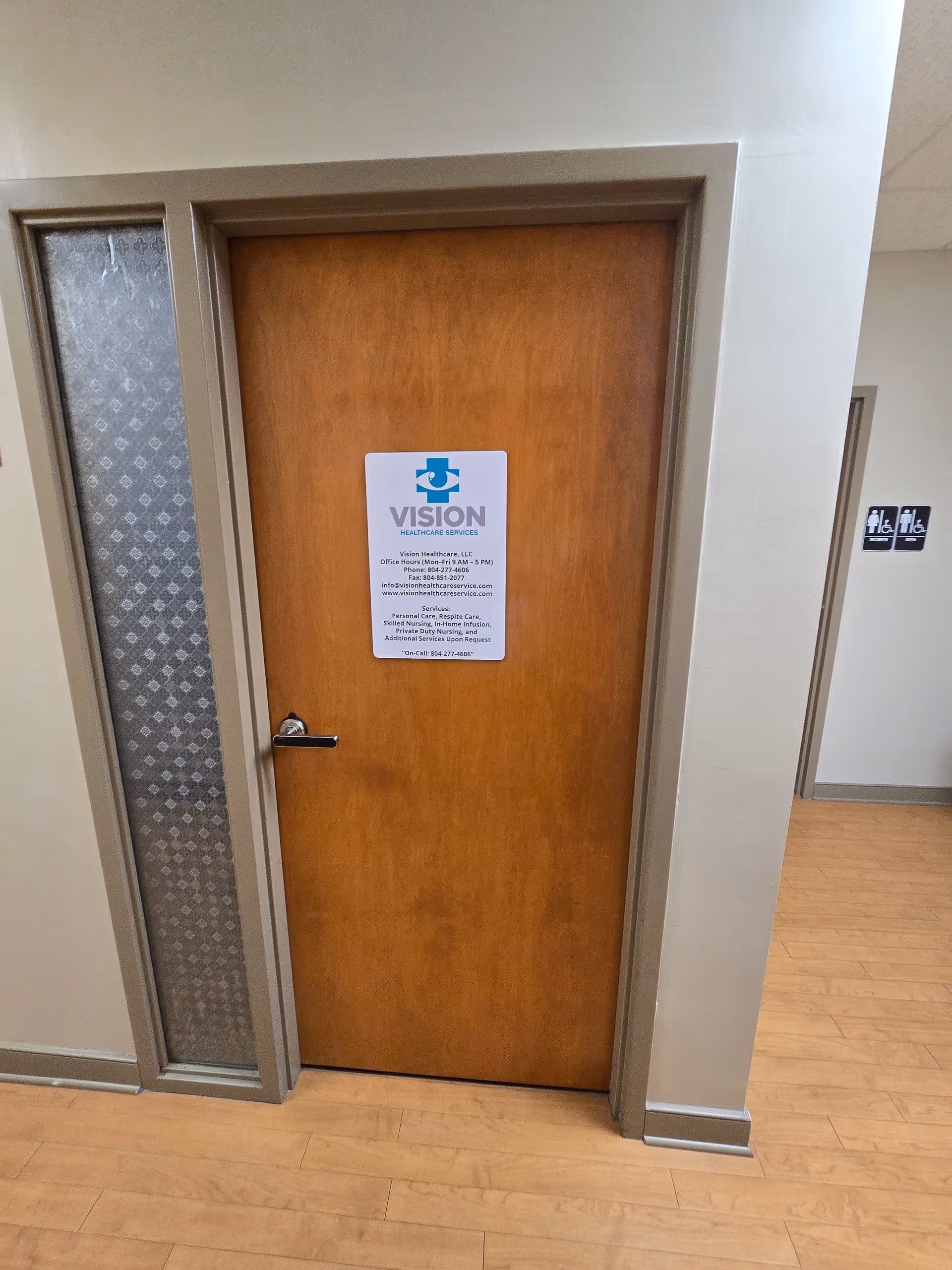 Wooden door with Vision Healthcare LLC sign in a corridor of a facility.