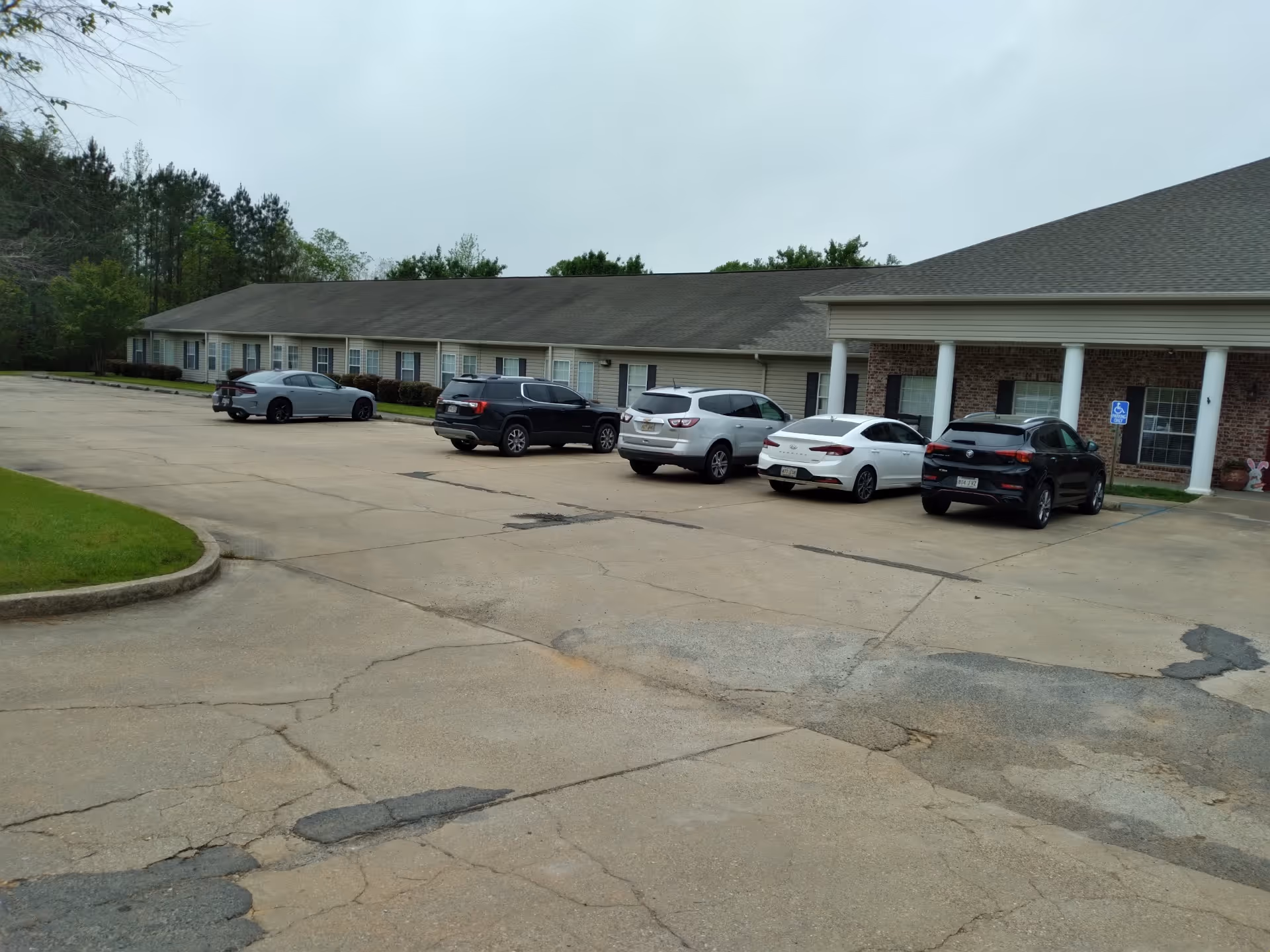 Single-story assisted living building with a long parking lot and several parked cars.