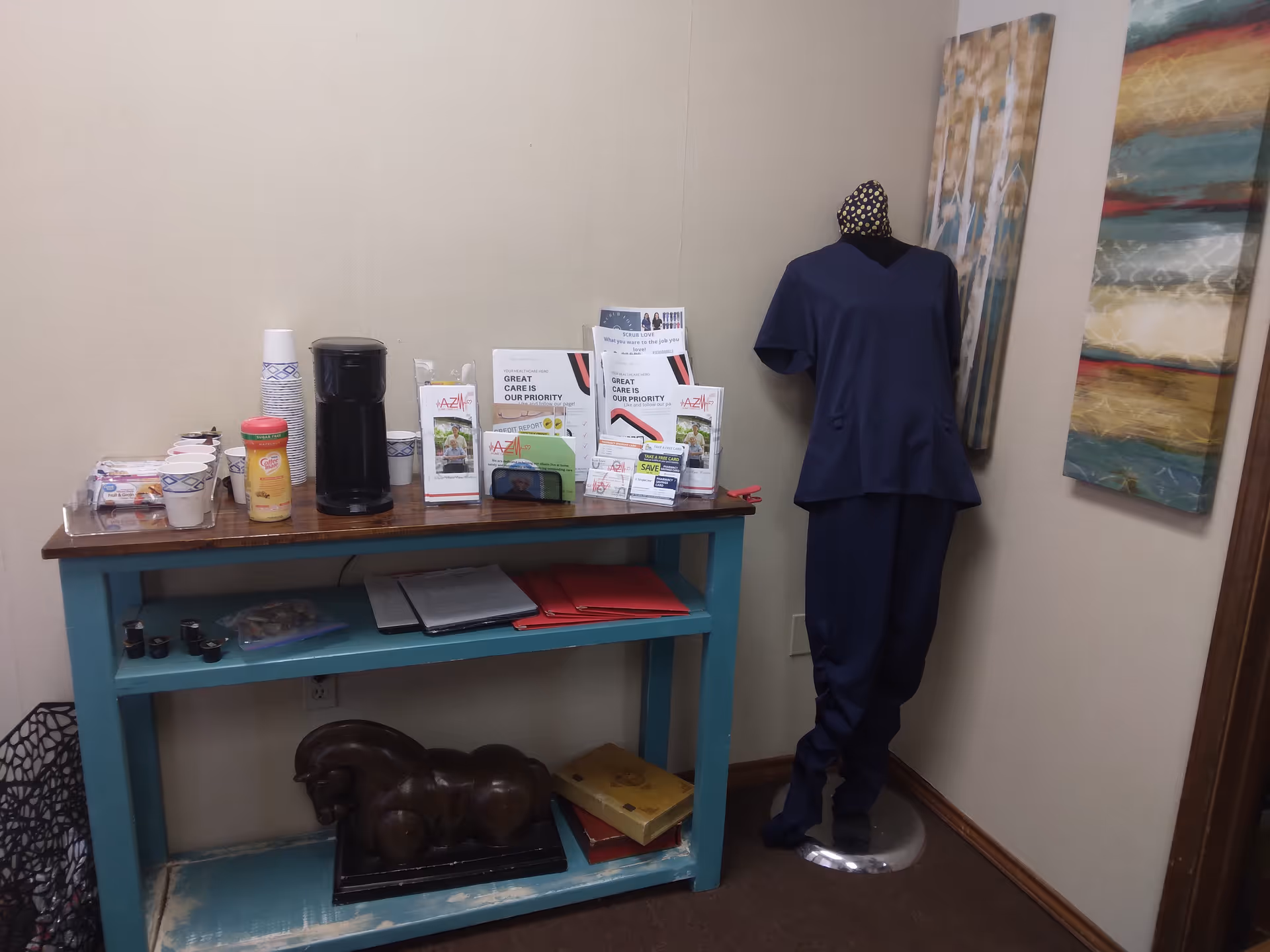 Teal table with brochures, coffee station, and a mannequin in scrubs.