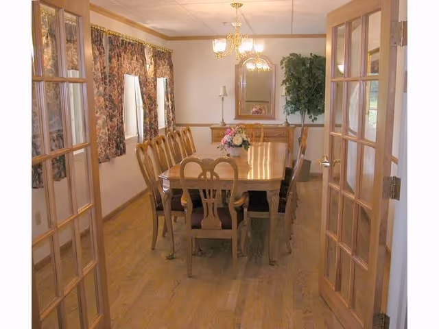A dining table with chairs, floral centerpiece, chandeliers, and curtains in a senior living dining room.