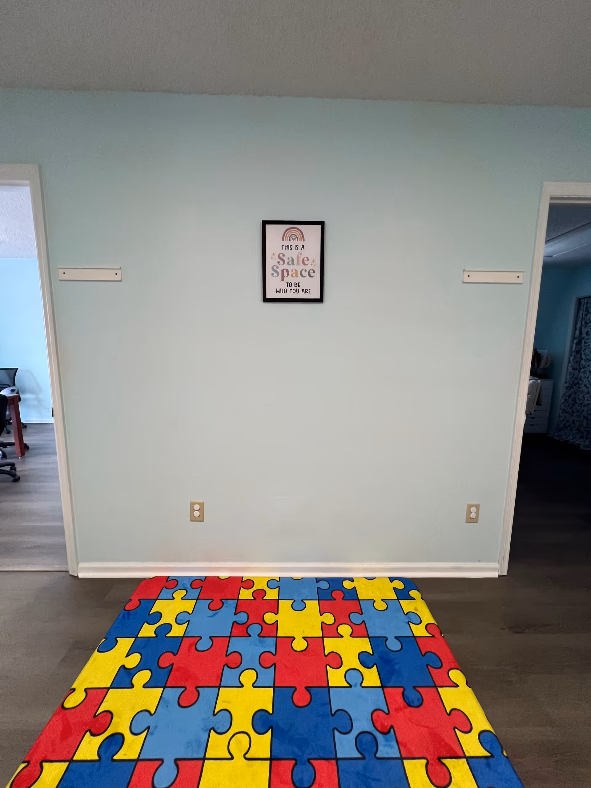 Light blue wall with a colorful puzzle mat on the floor and two doorways.