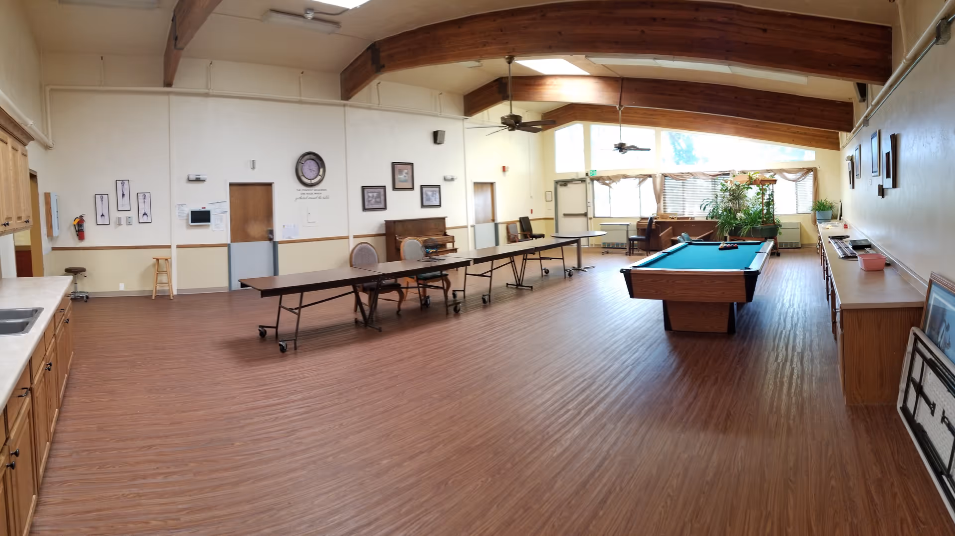 Spacious senior living recreation room with pool table, long tables, and wood beams.
