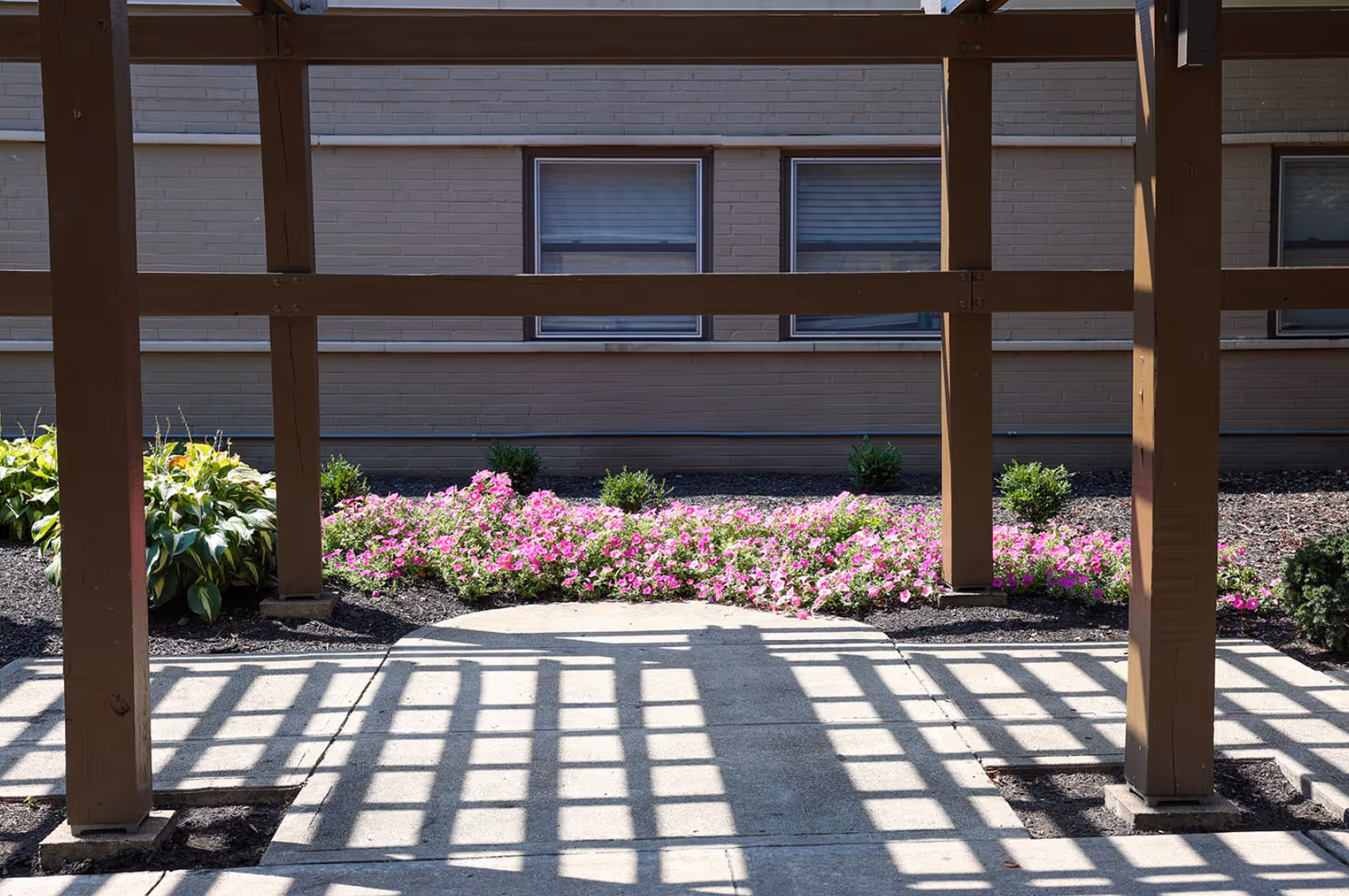 Exterior view of Pleasant Ridge Healthcare Center with a walkway under a wooden pergola and flowers.