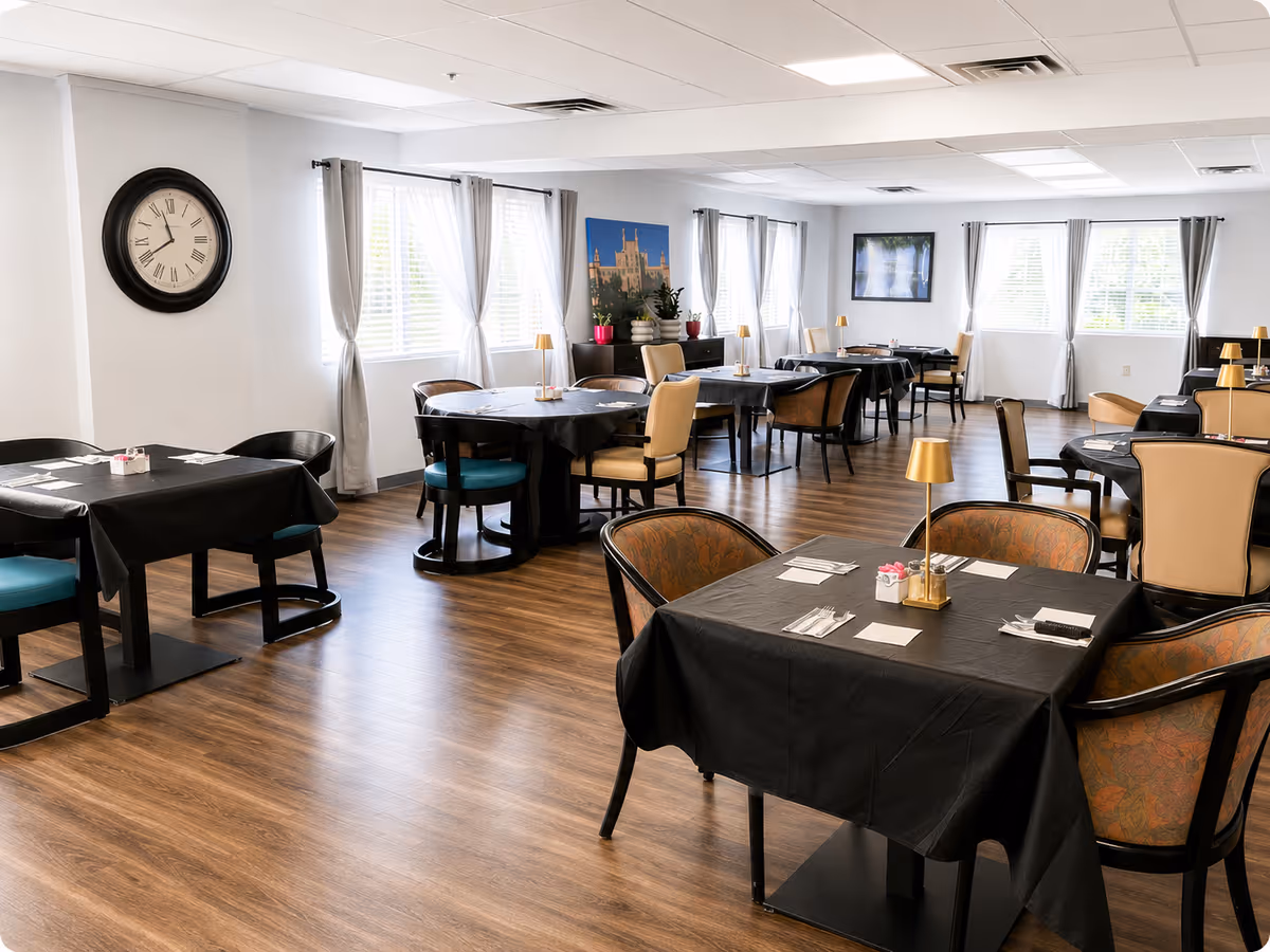 Bright dining room with black-cloth tables, chairs, windows with curtains, and a clock on the wall.