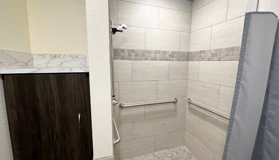 Accessible bathroom with tile shower, grab bars, and a privacy curtain.