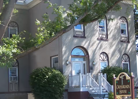 Two-story beige building with arched windows, entry stairs, and a Crossroads House sign.