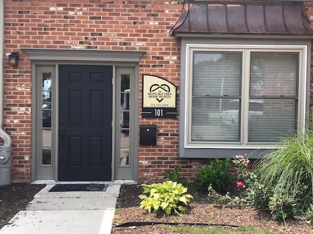 Brick building entrance with dark door and No Place Like Home Health sign.