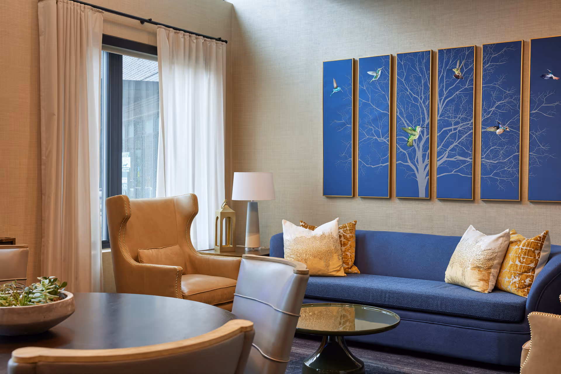 Cozy senior living lounge with blue sofa, beige armchair, and wall art.