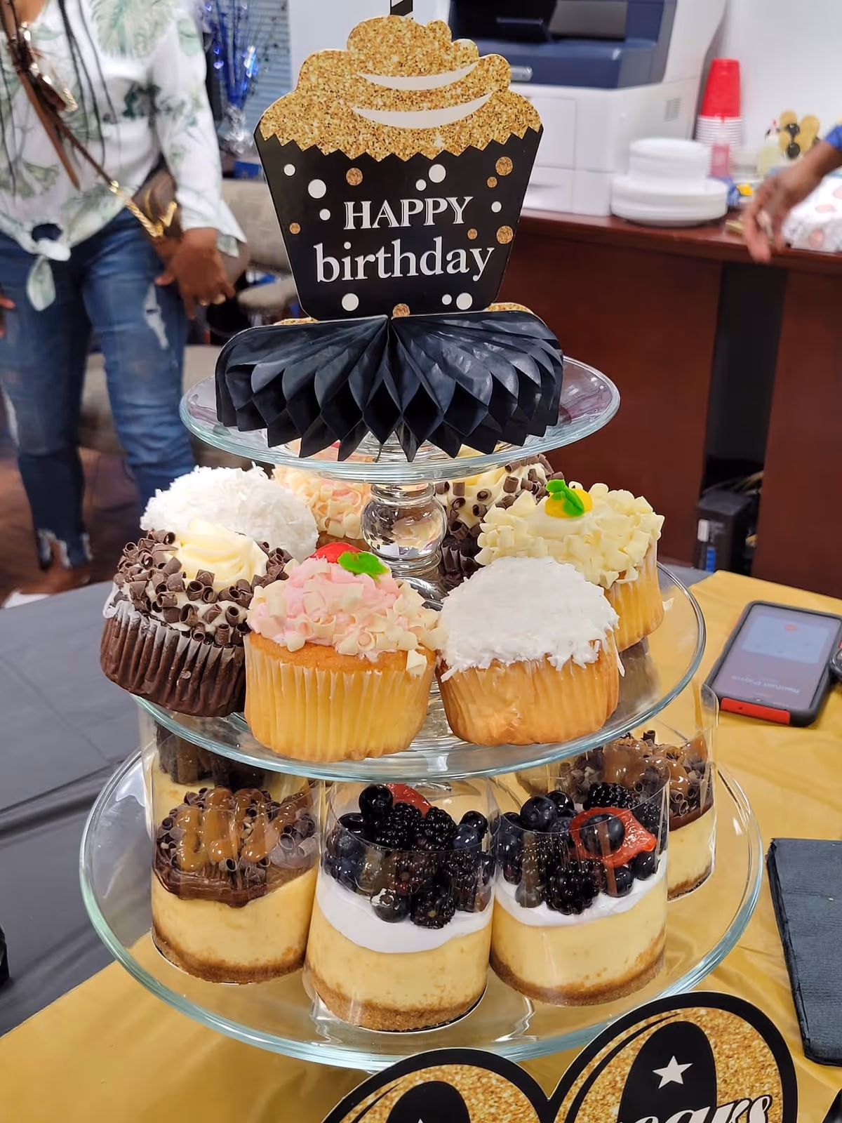 Tiered cake stand with assorted cupcakes and a birthday sign.