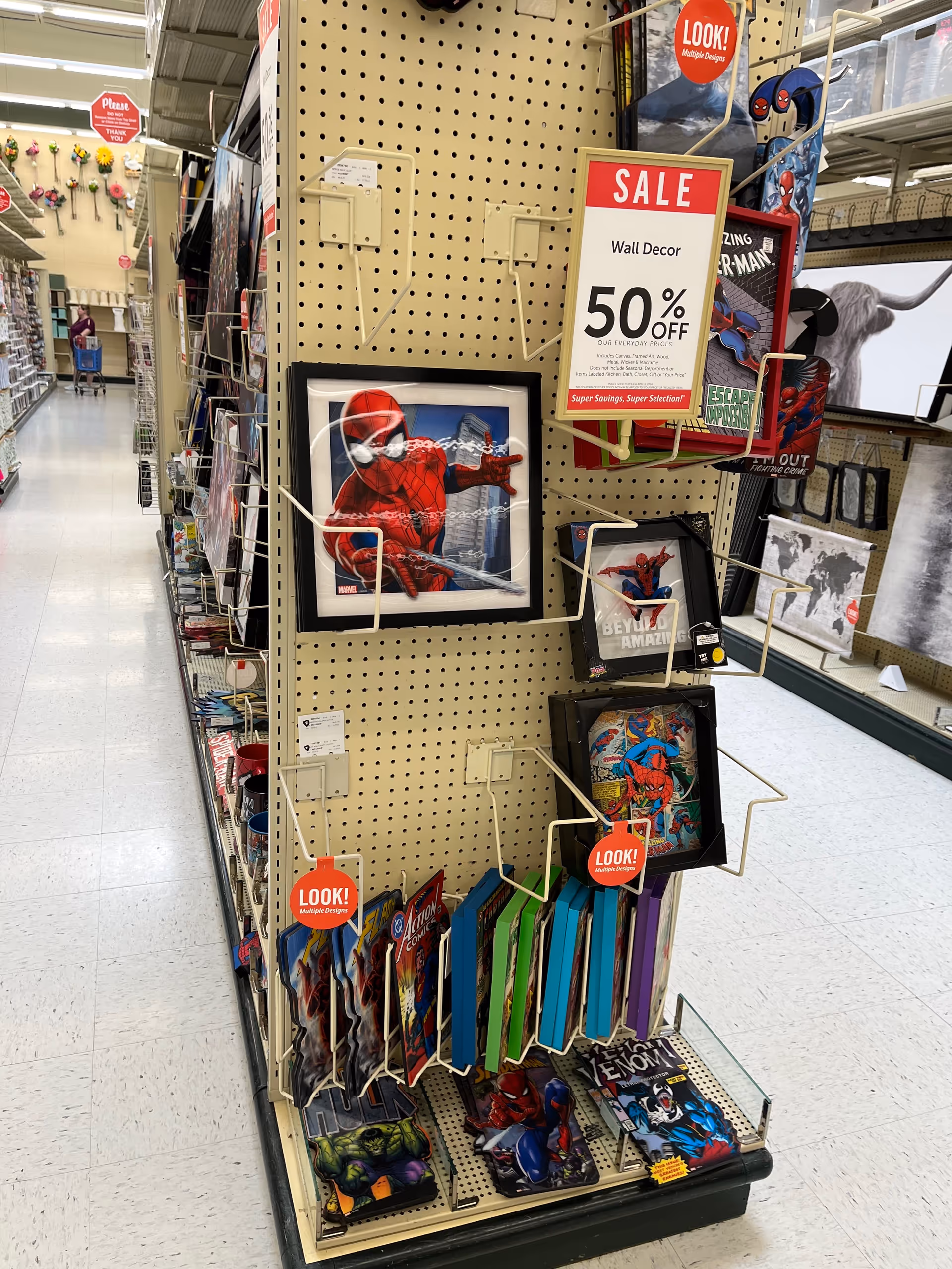 Retail aisle display with Spider-Man framed art on pegboard and sale signs.