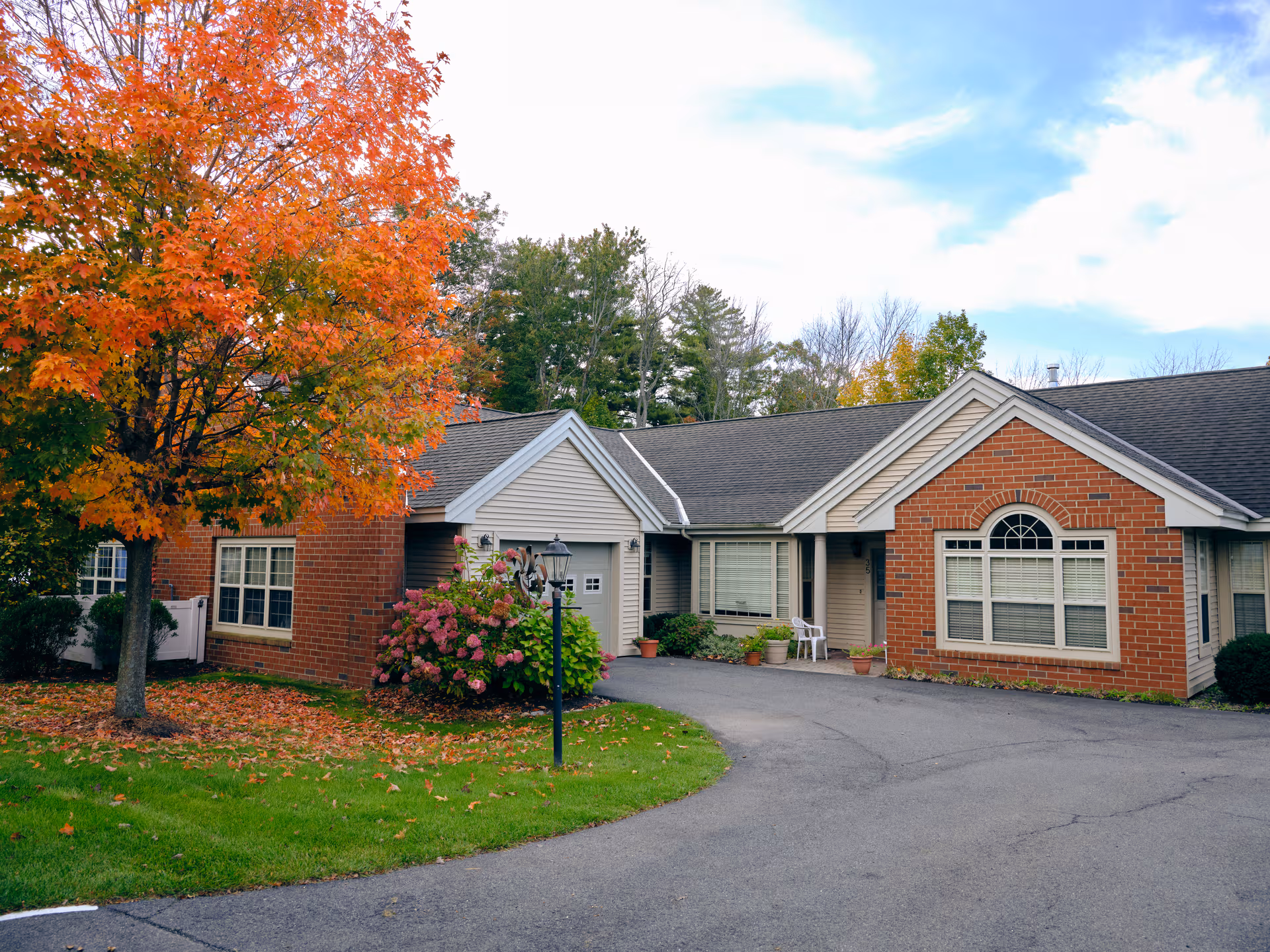 Single-story brick senior living facility exterior with autumn trees and a curved driveway.