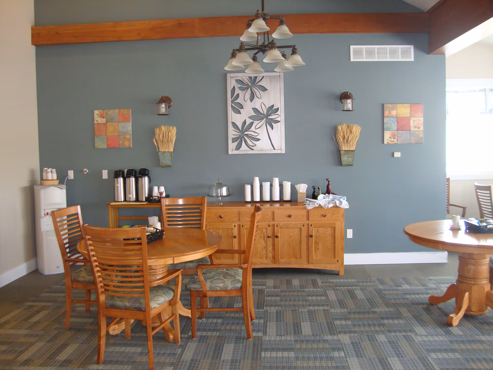 Wooden dining area with round table, chairs, and a coffee station against blue wall.