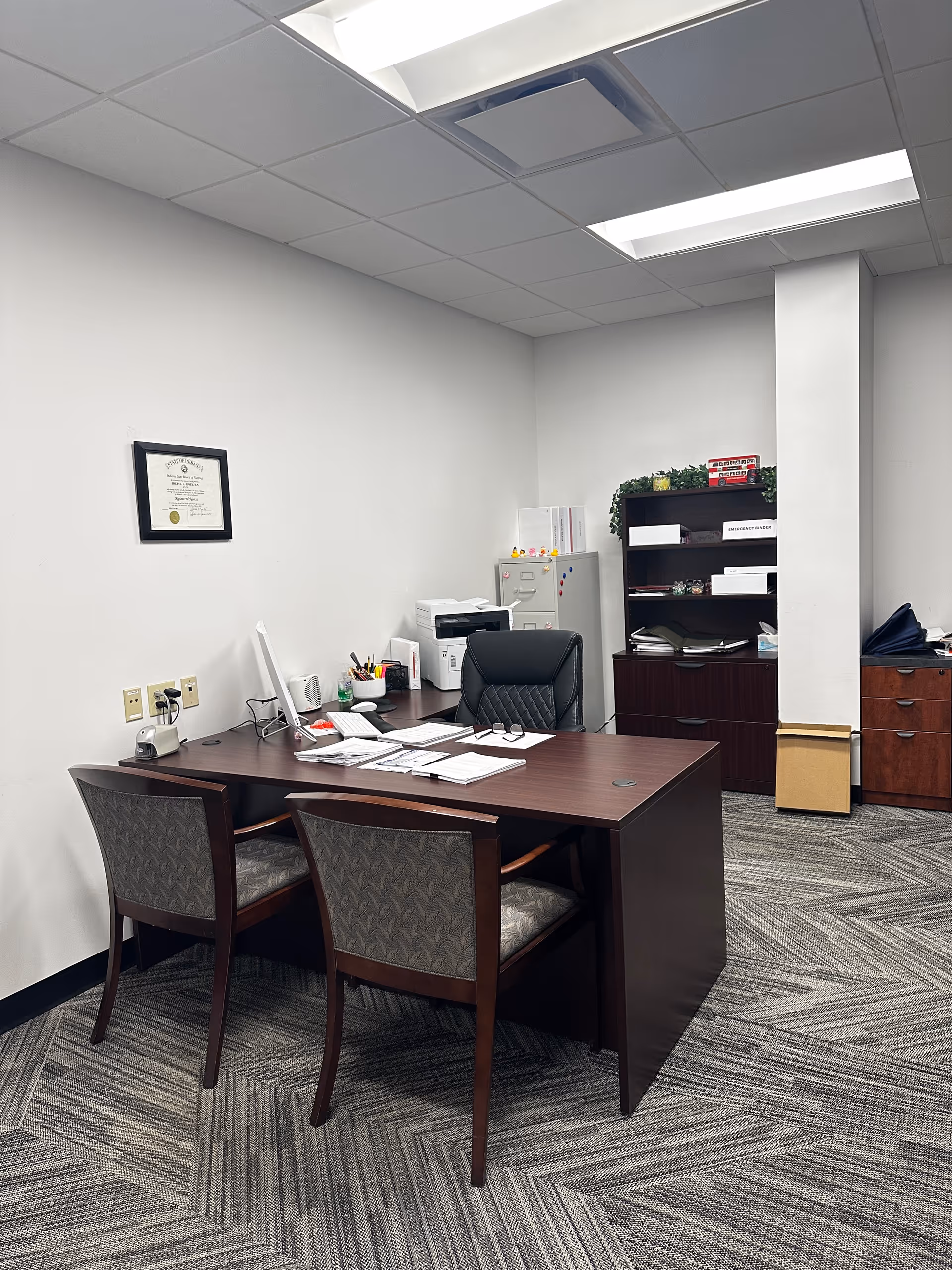 Administrative office with desk, chairs, printer, and shelves in a neutral workspace.