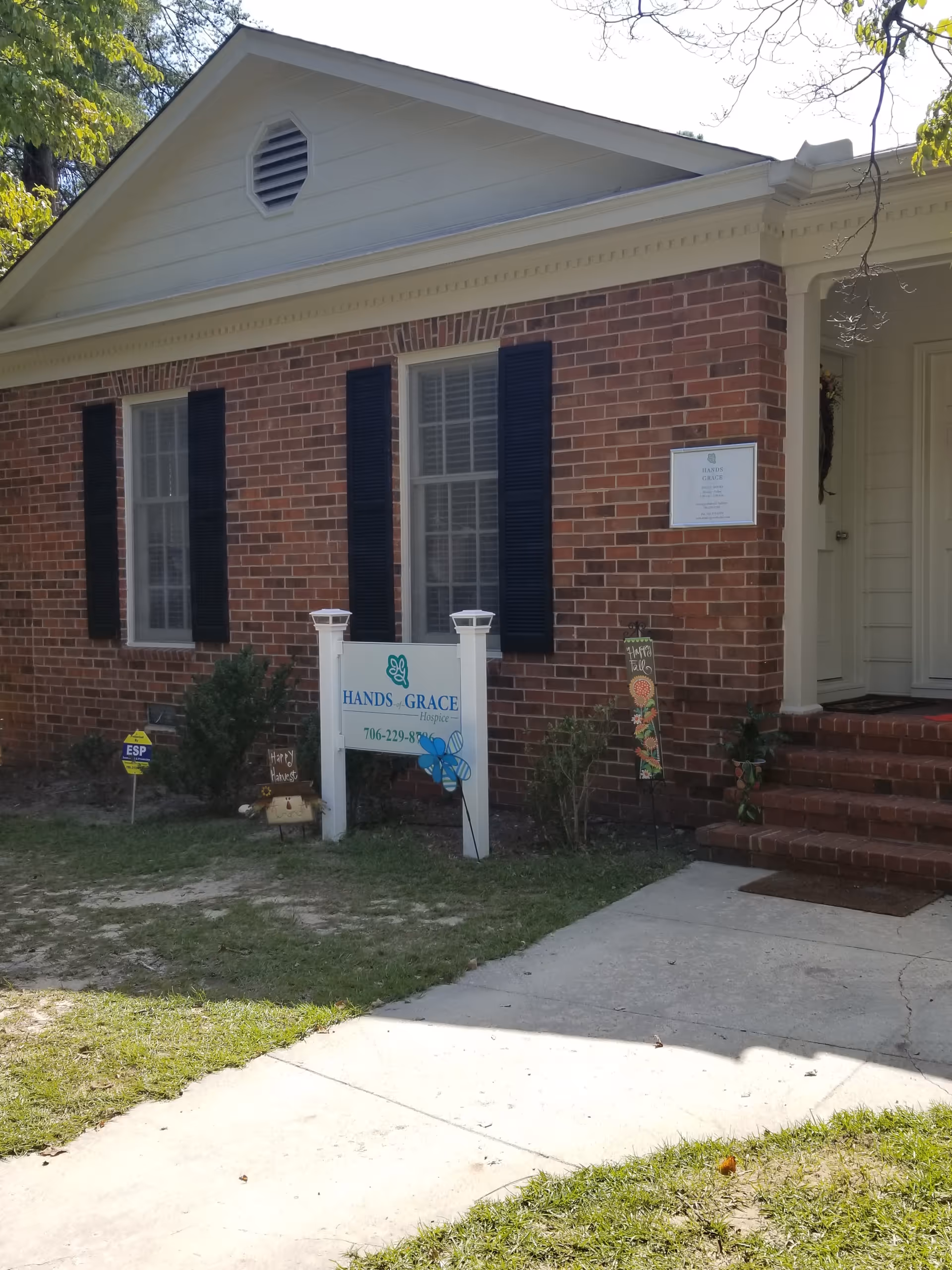 Brick hospice building with white trim, black shutters, and Hands of Grace sign at entrance.