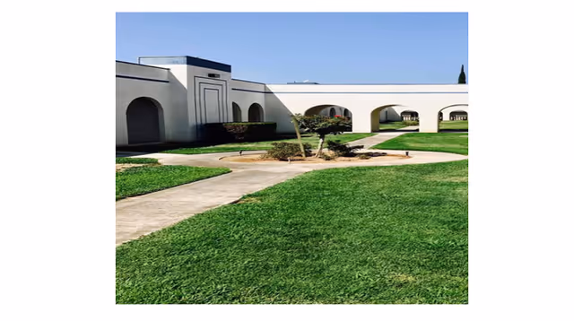 White retirement center exterior with arches, curved walkway, and circular garden on a sunny day.