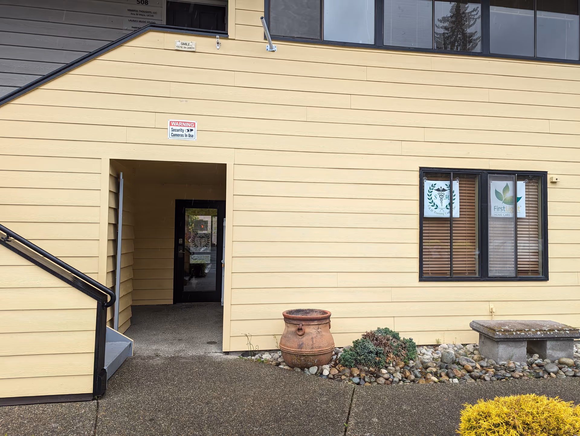 Beige building exterior with entrance doorway, window, and rock landscaping.