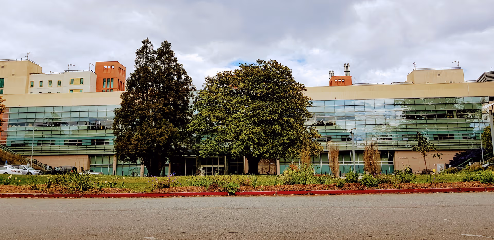 Front view of Laguna Honda Hospital with glass facade and trees along the street.