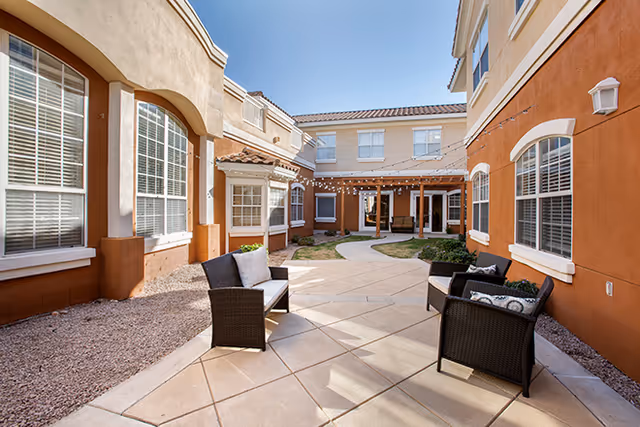 Outdoor courtyard with wicker seating, string lights, and apartment-style buildings.