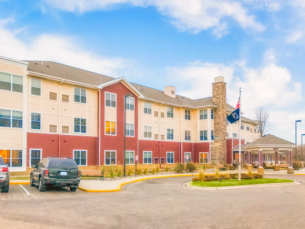 Extensive senior living facility exterior with a red-and-cream facade, driveway, and flagpoles.