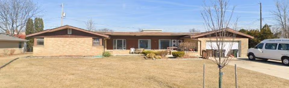Front exterior of a single-story brick senior living facility with driveway and a van