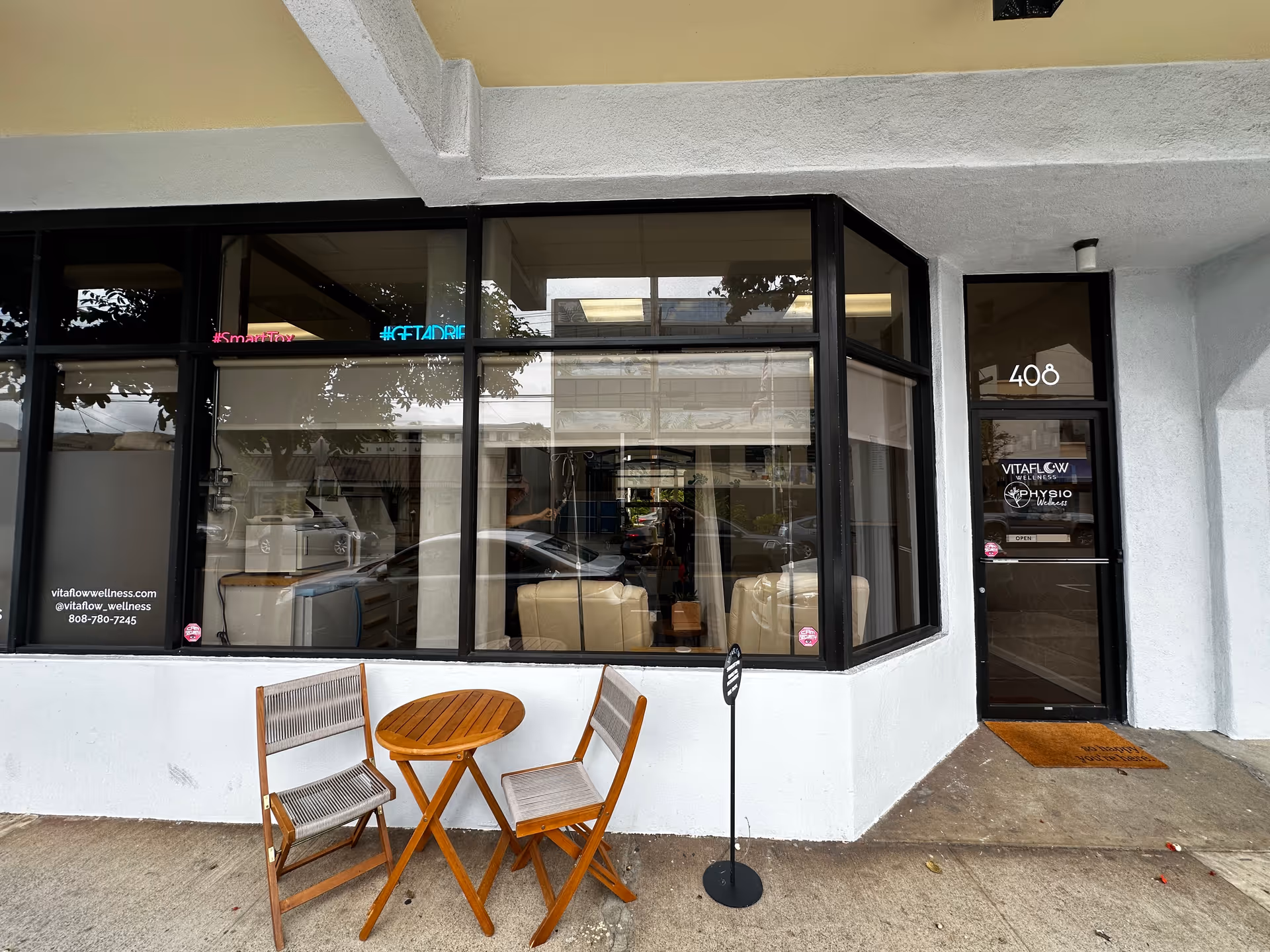 Storefront of Physio Wellness with glass windows, door labeled 408, and outdoor seating.