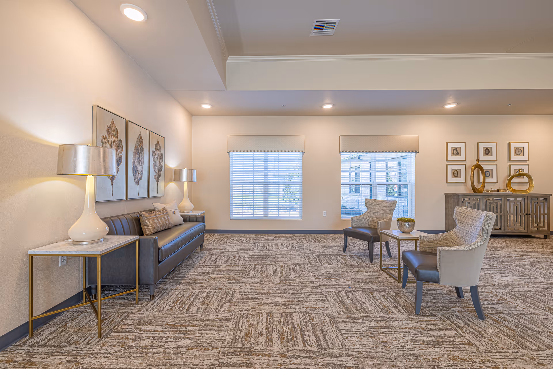 Bright lounge area with sofa, chairs, lamps, and large windows in neutral tones.