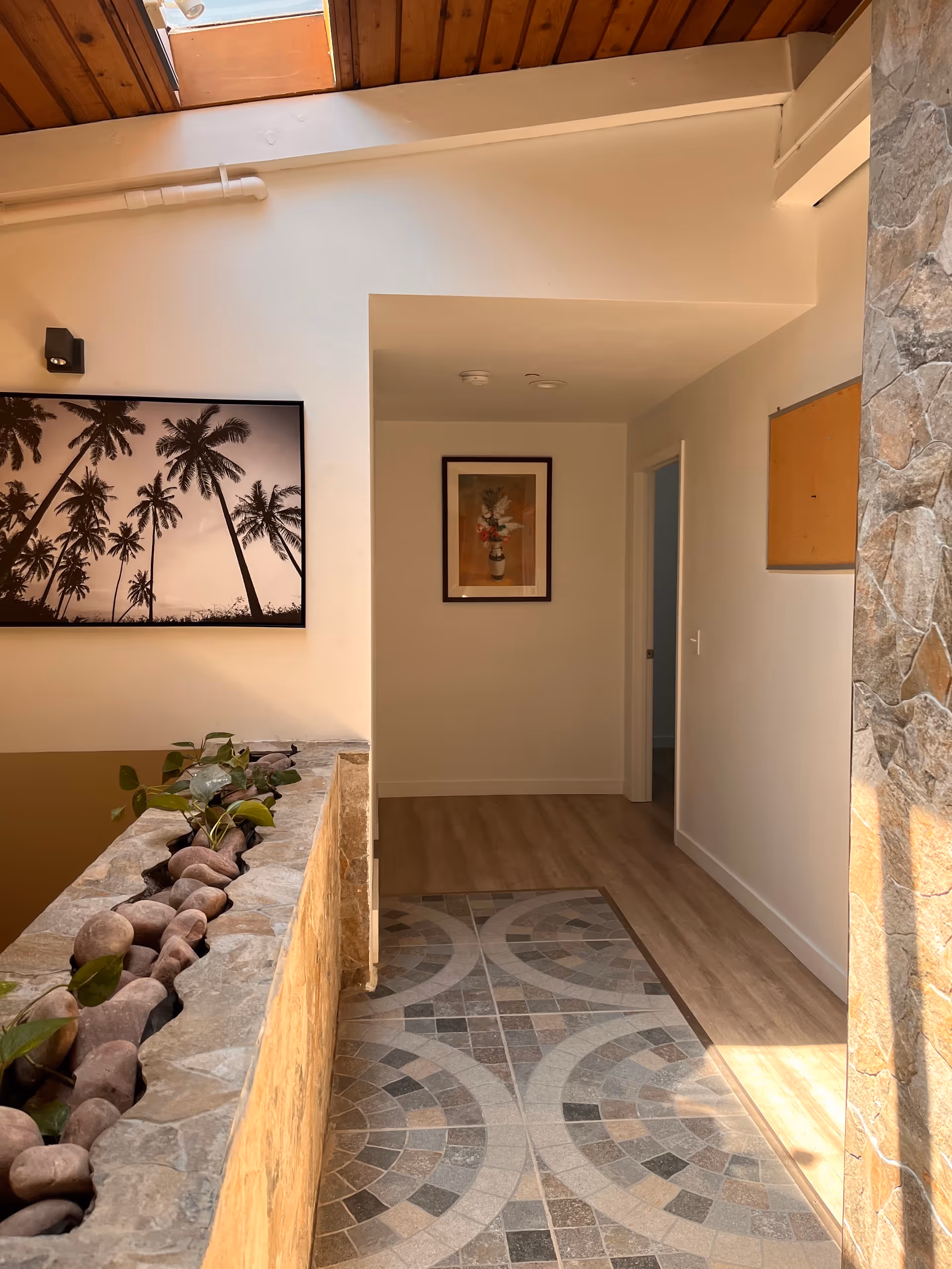 Indoor hallway with mosaic-tiled floor, stone planter, and framed art on the walls.
