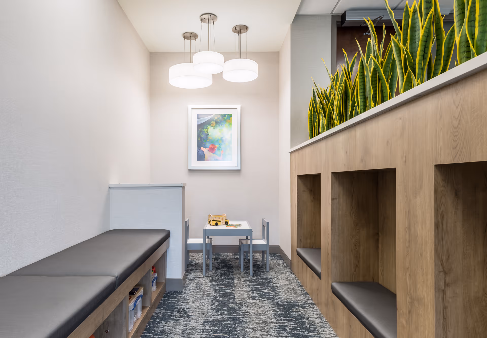 Bright, modern therapy waiting area with bench seating, cubby shelves, a small table, and plants.