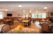Spacious dining room with tables, chairs, and sunlit windows in a senior facility.