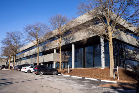 Front view of a modern office building with parked cars in a lot.