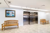 Lobby area with two wooden benches, framed artwork, and elevator doors.