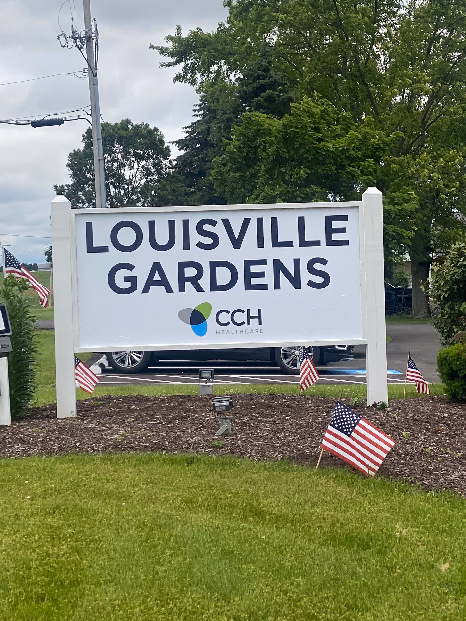 White sign reading Louisville Gardens with American flags and green lawn in front.