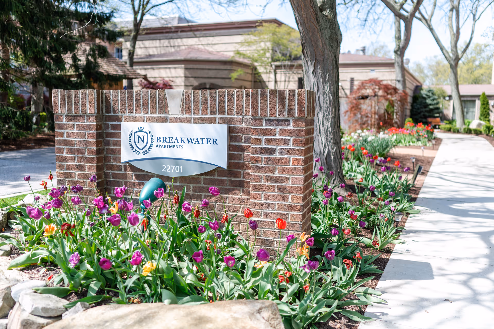 Brick entrance sign with Breakwater Apartments logo and a tulip-filled flower bed.