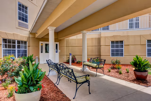 Covered entrance courtyard of a senior living building with benches, potted plants, and landscaping.