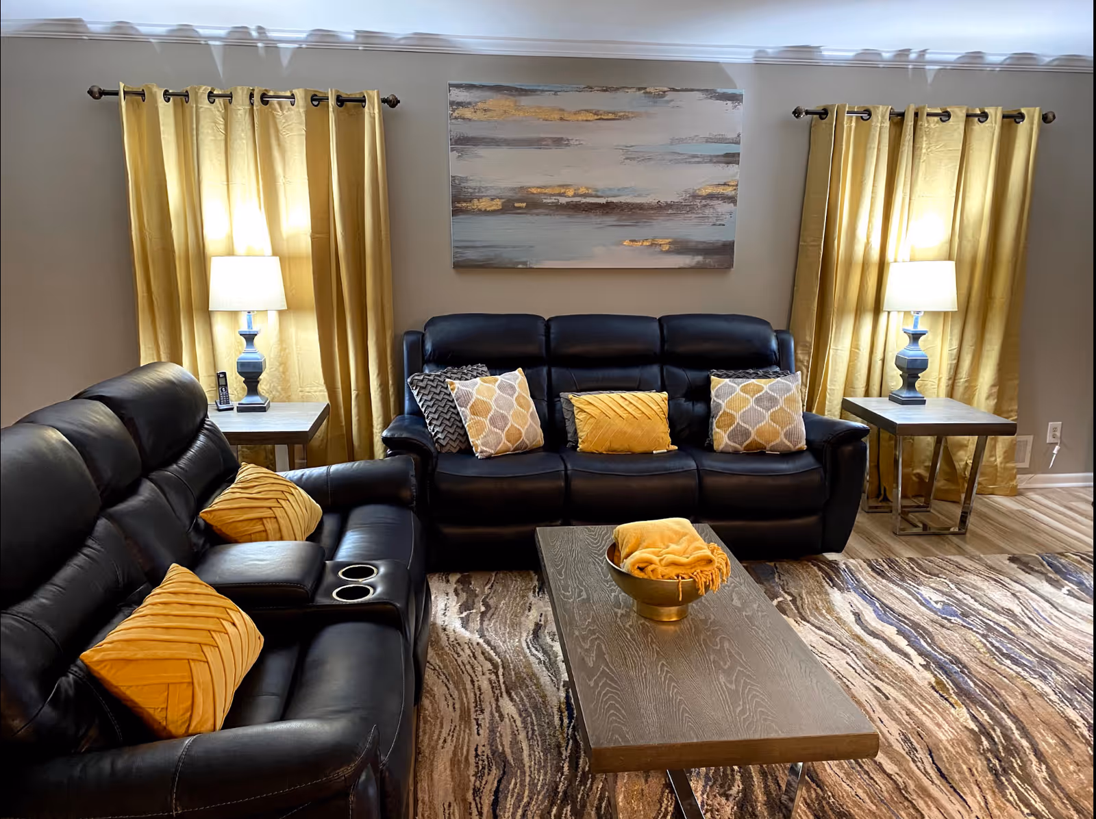 Cozy living room with black leather sofas, gold accents, lamps, and wall art.
