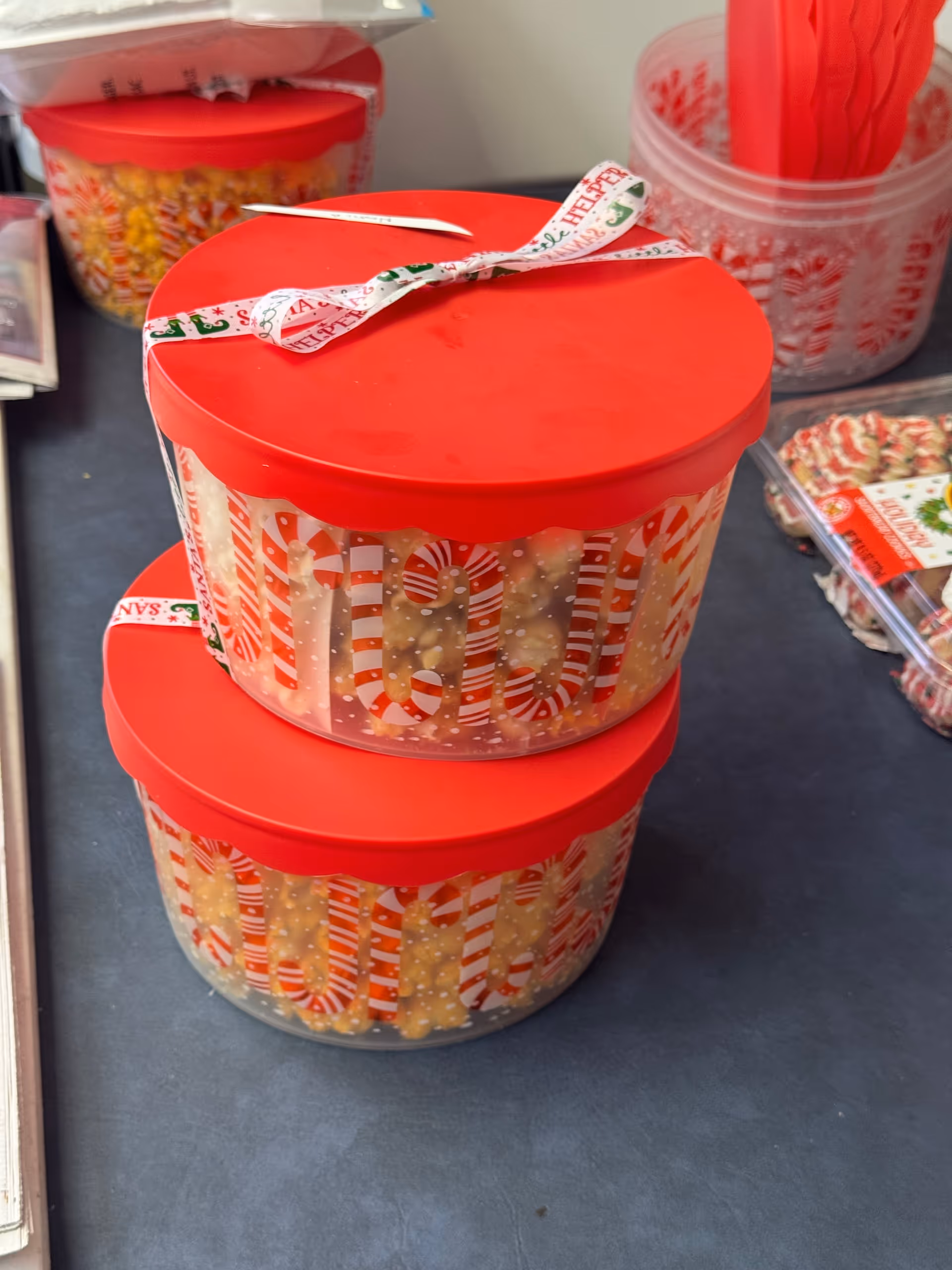 Two red-lidded candy jars with holiday-themed labels on a dark countertop.