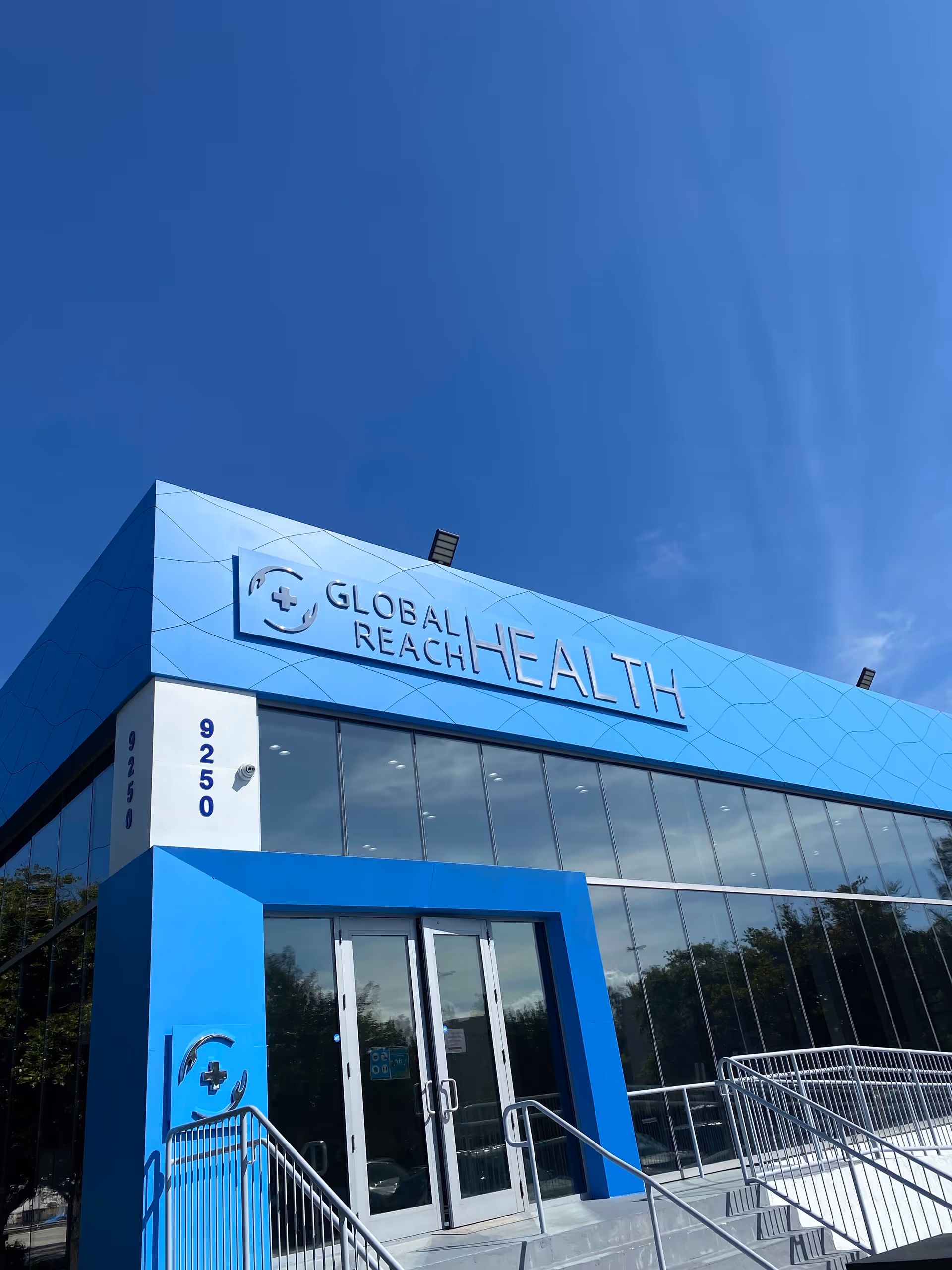Blue Global Reach Health building entrance with glass windows and stairs.