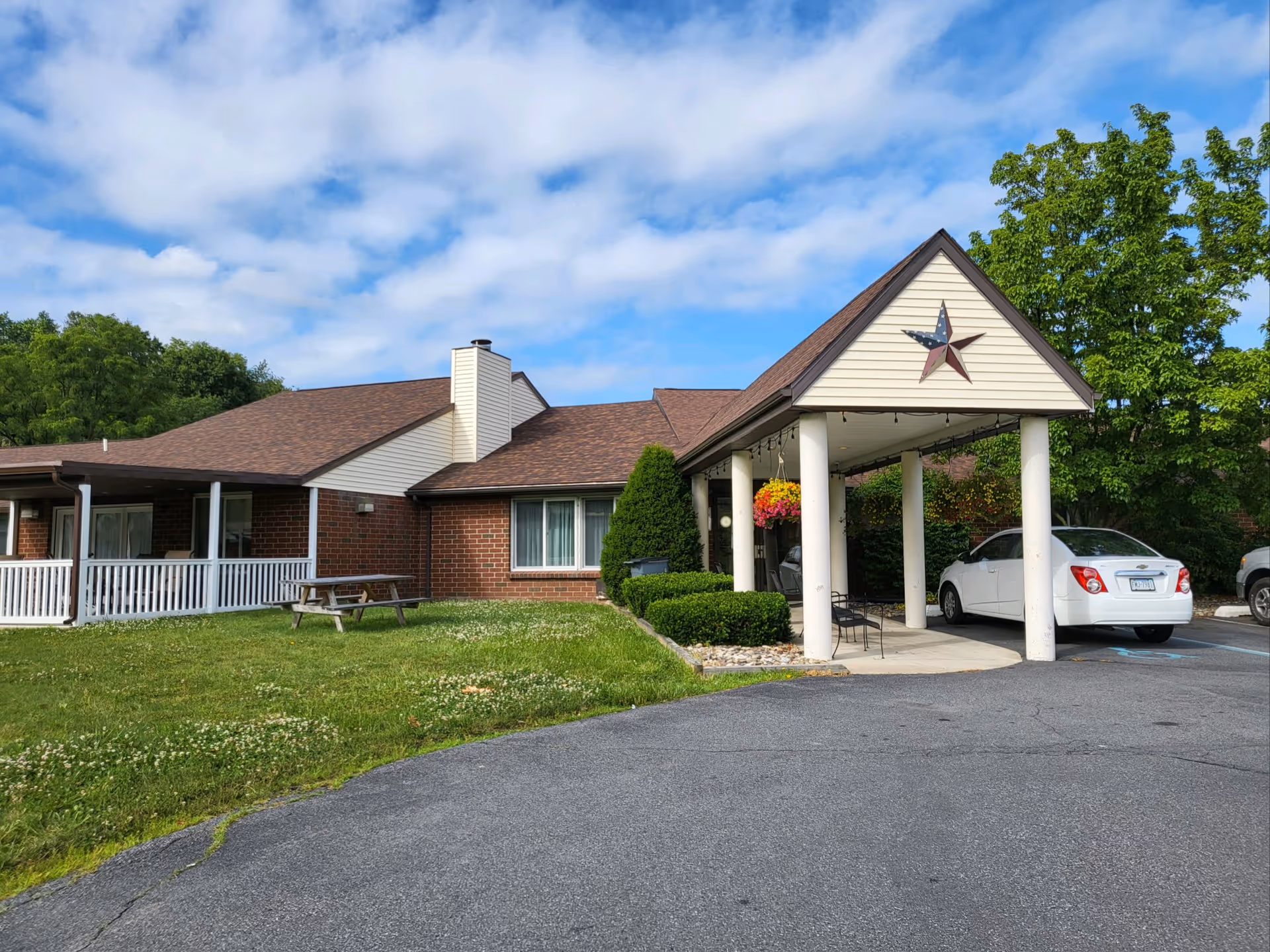 Senior living facility exterior with brick building, covered entrance, cars, and manicured lawn.