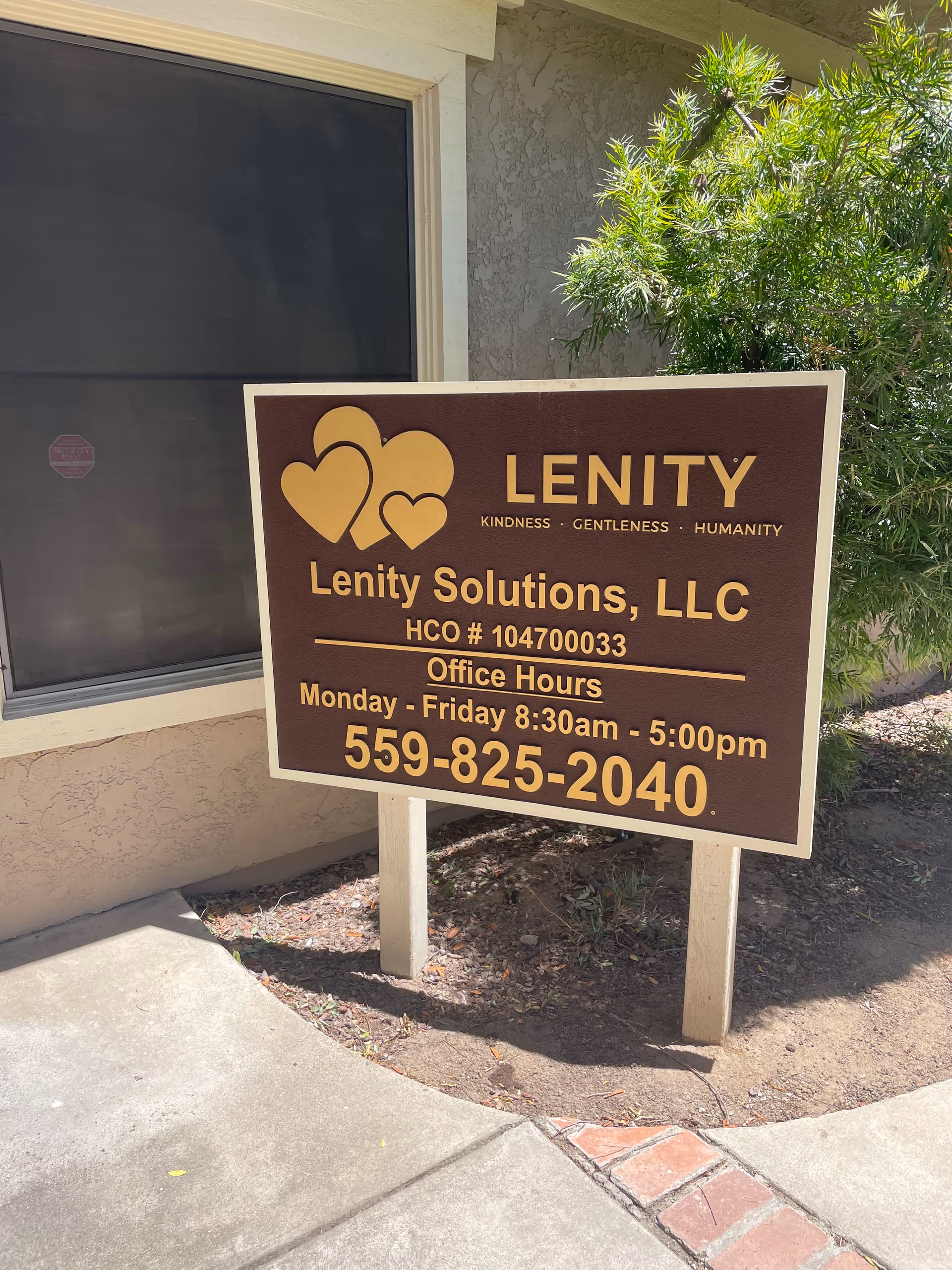 Brown Lenity Solutions sign outside a building with a window and greenery