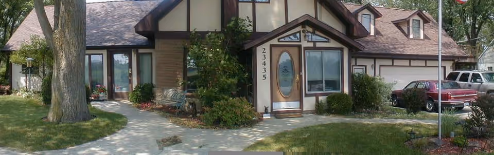 Exterior view of a suburban-style senior living facility with a front entrance and parked cars.