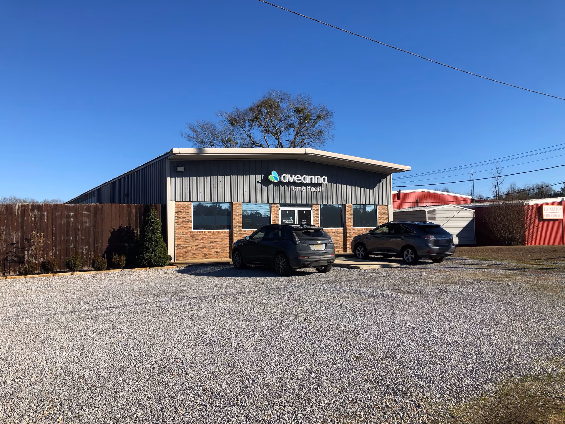A single-story Aveanna Home Health building with a gravel parking lot and two cars.