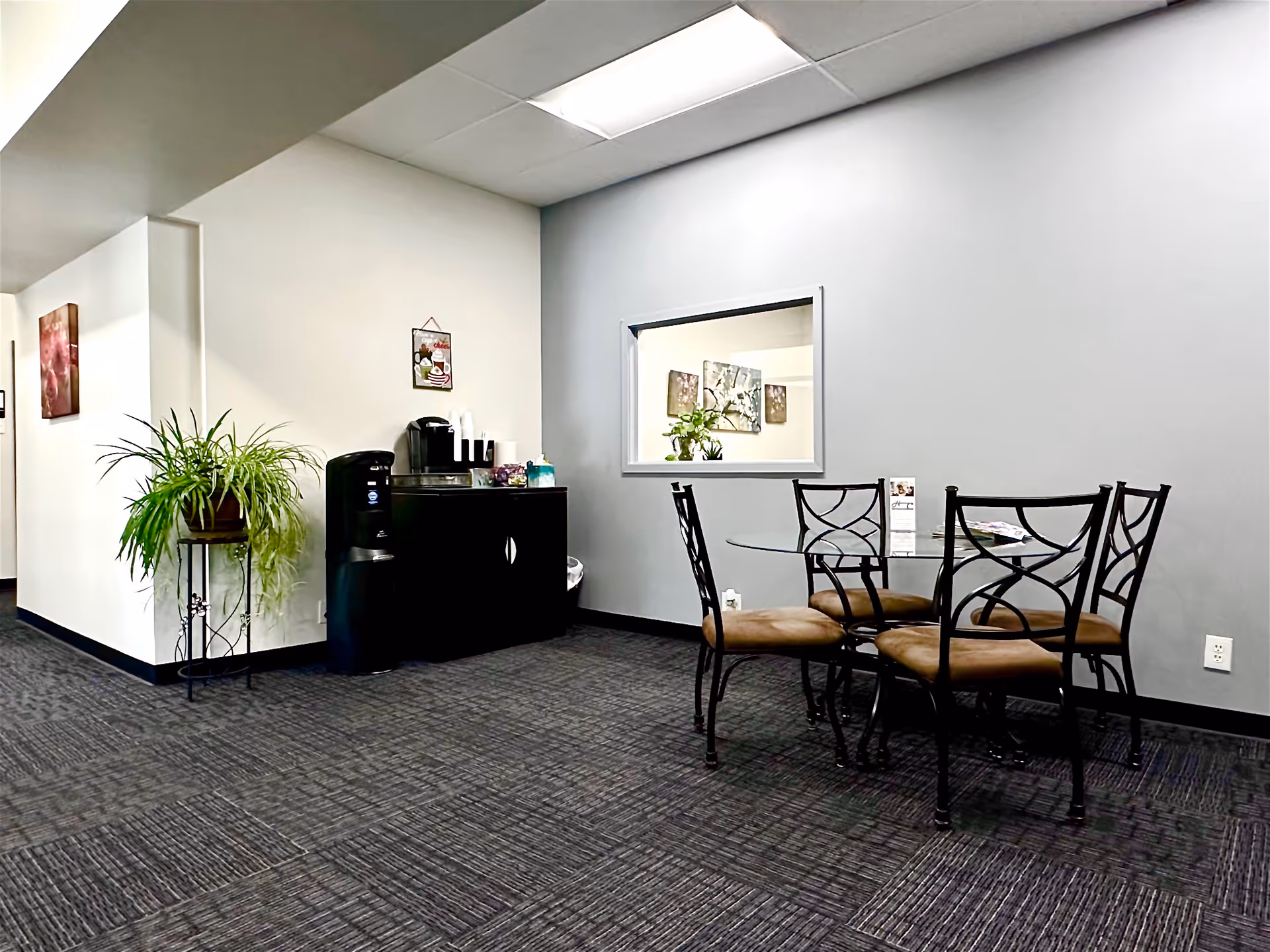 Interior dining area with a glass round table, metal chairs, a coffee station, and plants.