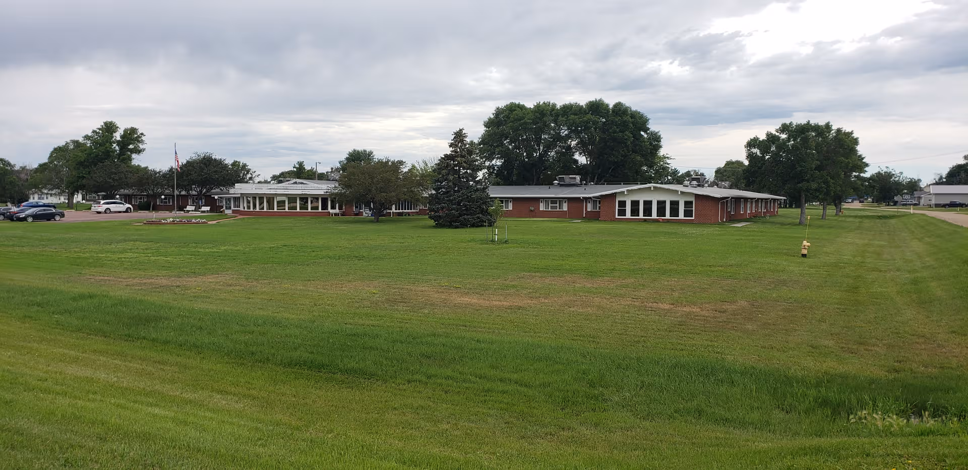 Wide shot of a brick nursing home with a large green lawn and parking area.