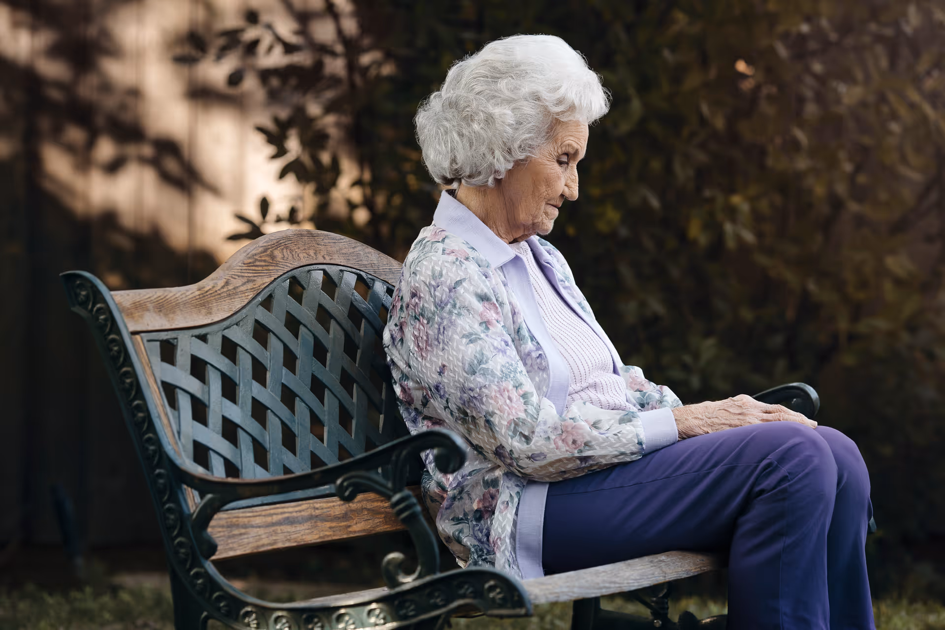 Elderly woman sits on a decorative outdoor bench in a garden.