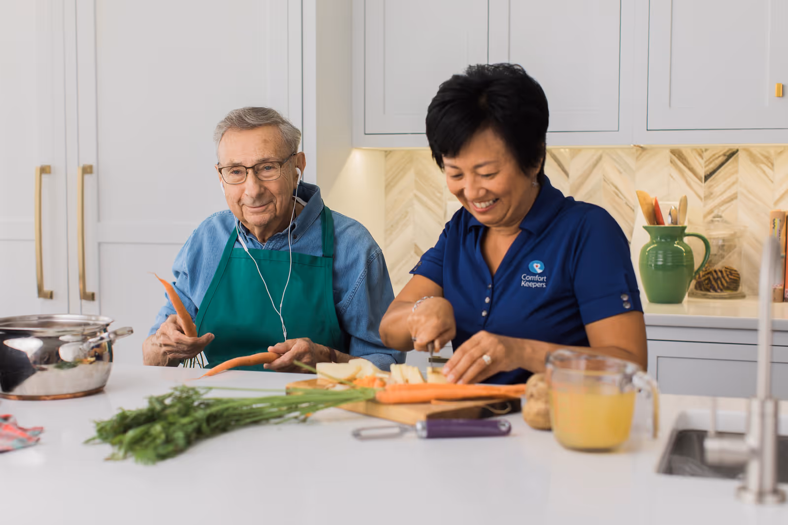 Two caregivers prepare vegetables together at a bright kitchen island.