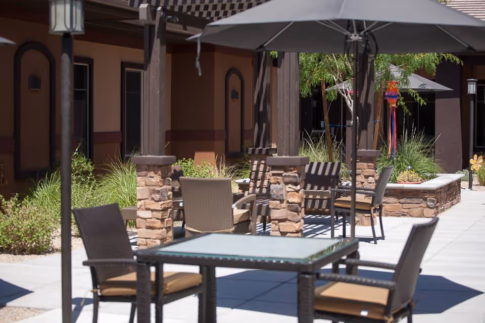 Outdoor patio with glass-top tables, chairs, and stone pillars at Golden Hearts Inc.