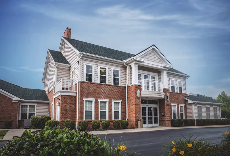 Front exterior of The Rutherford Memory Care building with brick, columns, and landscaping.