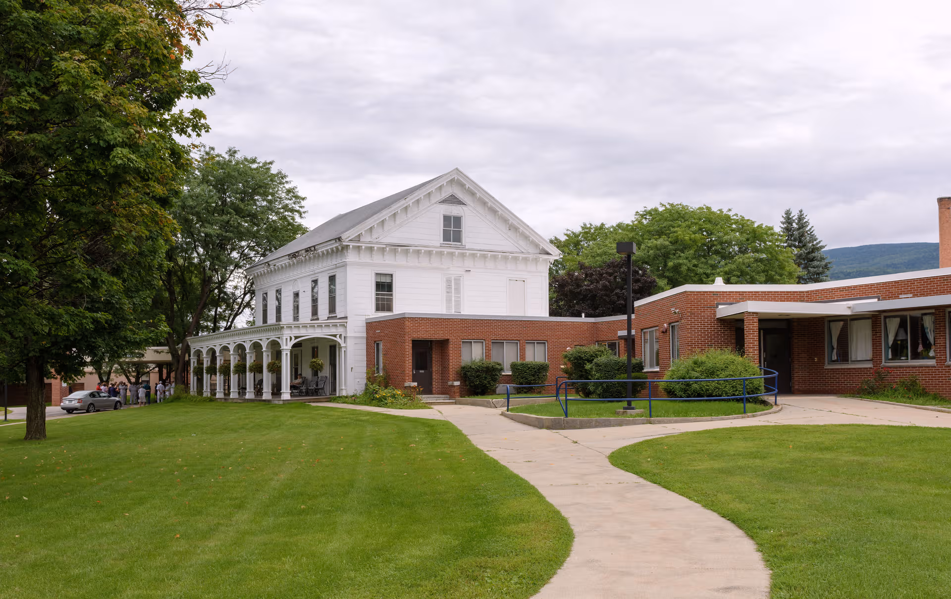 A large white brick senior living facility exterior with a curved walkway and green lawn.