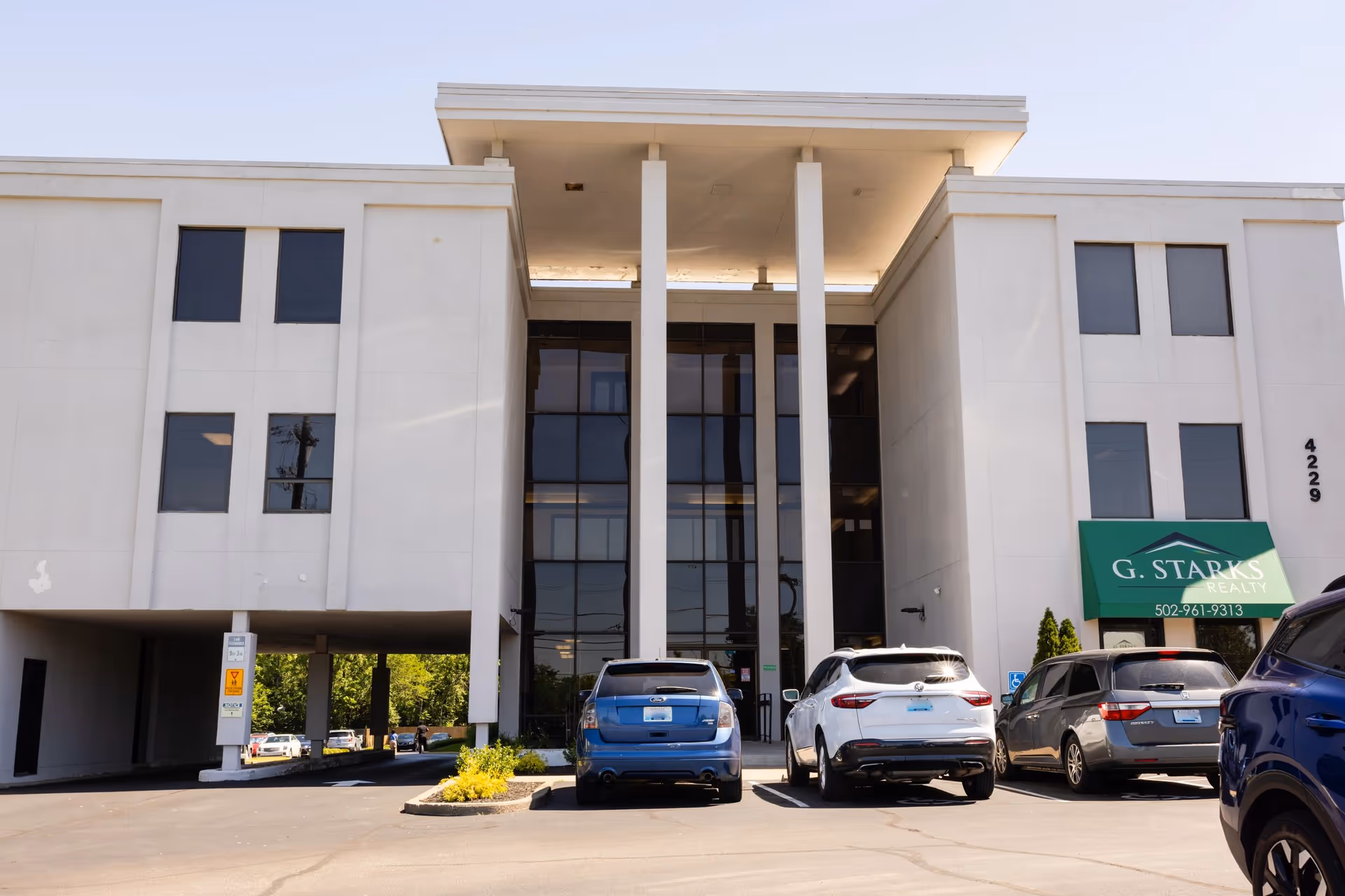 White modern building exterior with tall glass entrance and several parked cars.