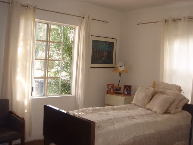 Cozy bedroom in a senior living facility with a bed, nightstand, lamp, and window.